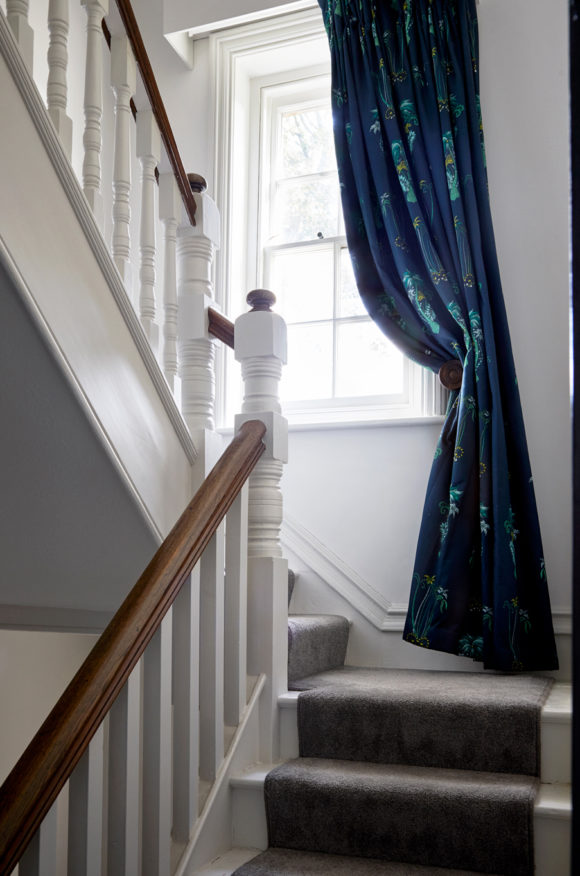 staircase with grey carpet, draped blue patterned curtains